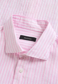 Chemise pour homme à rayures verticales roses et blanches, boutonnée, avec col replié et étiquette noire "Matinique" à l'intérieur du col.