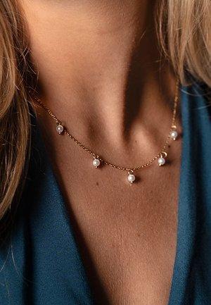 Collar de cadena dorada con pequeñas perlas blancas espaciadas de manera uniforme a lo largo de la longitud. Textura suave y diseño delicado, reposando sobre la clavícula.