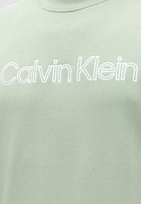 Sweat-shirt vert clair col rond avec texte brodé blanc "Calvin Klein" sur la poitrine.