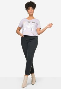 Lavendel T-shirt met korte mouwen met zilveren hartgraphics, gecombineerd met strakke zwarte jeans met zijknopaccenten en beige enkellaarzen.