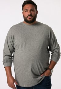 Camiseta gris de manga larga en tejido suave con cuello redondo y un pequeño logo en el pecho, combinada con jeans de mezclilla azul.