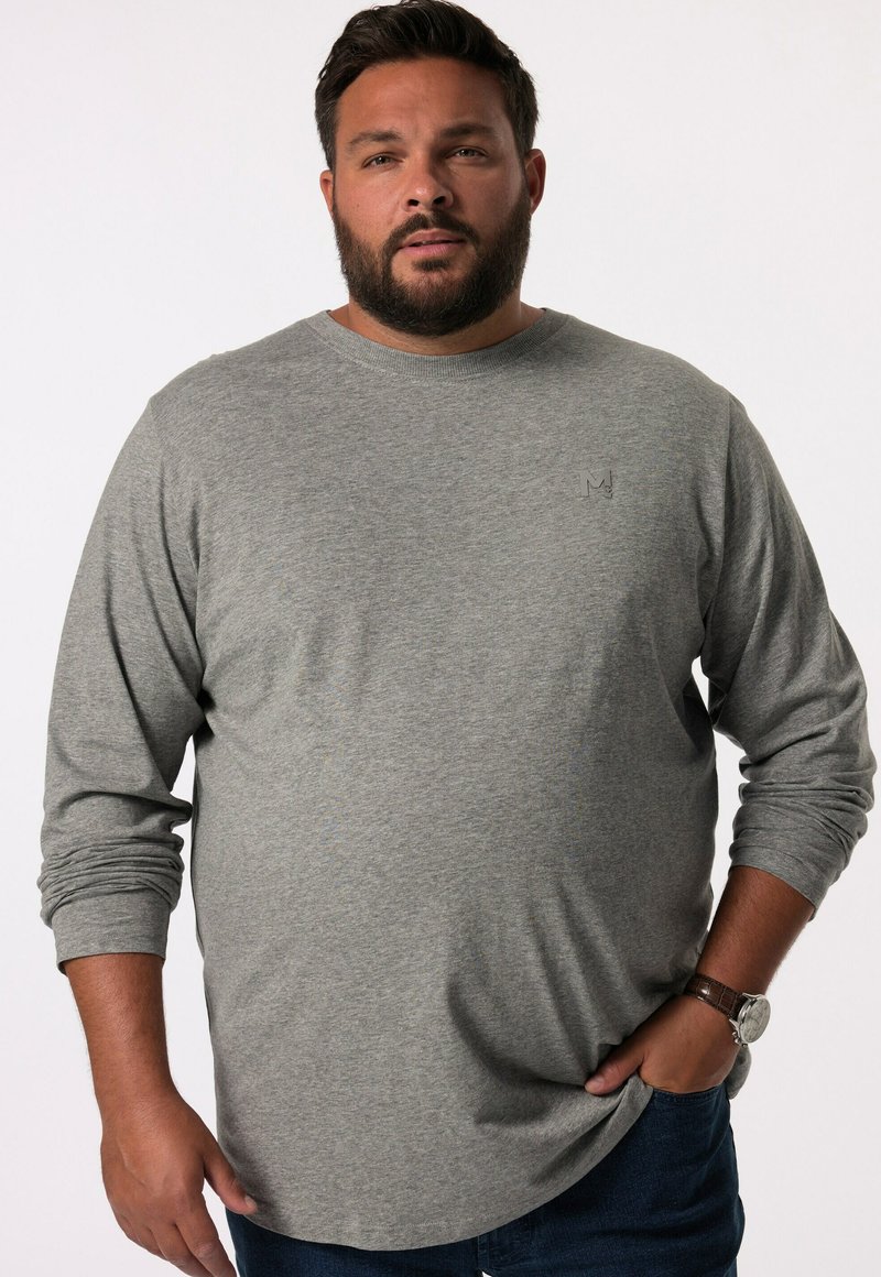 Camiseta gris de manga larga en tejido suave con cuello redondo y un pequeño logo en el pecho, combinada con jeans de mezclilla azul.