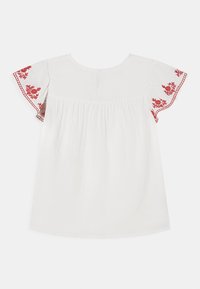 Top bianco con ricami floreali rossi sulle maniche corte, caratterizzato da una scollatura rotonda e una schiena plissettata per una vestibilità comoda.