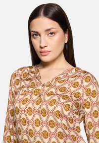 Blusa a maniche lunghe in rosa chiaro con un motivo floreale che presenta fiori marroni e arancioni. Collo con bottoni, tessuto morbido, stoffa leggera.