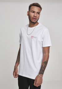 White cotton t-shirt with short sleeves, featuring red text design on the chest. Paired with black pants and simple gold chain.