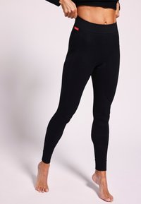 Leggings noirs en tissu texturé, dotés d'une taille haute élastique et de jambes ajustées, avec un petit logo rouge sur le côté.