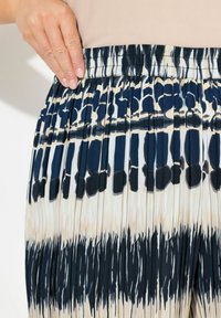 Plisserad kjol i tyg med elastisk midja. Har ett mönster av mörk marinblå och krämfärgade abstrakta former som smälter samman. Mjuk textur.