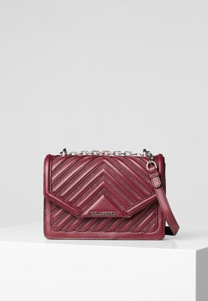 Sac bandoulière en cuir matelassé bordeaux avec bandoulière chaîne argentée et fermeture à rabat, placé sur un piédestal blanc sur fond gris clair.