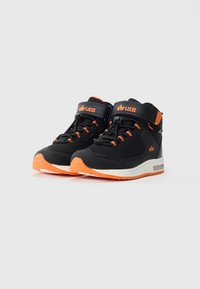 Tênis high-top LICO preto e laranja com faixas de Velcro, cadarços com puxador, e solas brancas sobre um fundo claro.