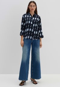 Marineblauw shirt met een lichtblauw abstract patroon, knoopsluiting aan de voorkant en driekwartmouwen. Gepaard met wijde blauwe jeans en zwarte hakken.