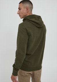 Olivenfarbener Hoodie aus weichem Material, mit Kordelzugkapuze, gerippten Bündchen und Saum sowie einem lässigen Schnitt. Schlicht, ohne sichtbare Muster.