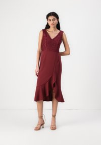 Burgundy színű, térd felett érő ruha csipke felső résszel, V-kivágással és fodros szegéllyel. Jellemzője a karcsú derék és a sima textúra.