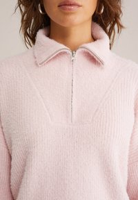 Gaiši rozā flīsa pusvilnas krekls ar mīkstu tekstūru, ribota paneļa dizainu un sudraba rāvējslēdzēja detaļu apkaklē.