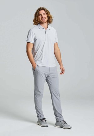 Jasnoszara koszulka polo, slim fit, z krótkim rękawem; zestawiona z dopasowanymi jasnoszarymi spodniami. Buty są szare z czarnymi akcentami i sznurówkami.