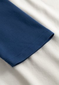 Puuvillane T-särk tumesinise varruka ja kergekreemika kehaosaga, millel on sile tekstuur ja korralik ääreliist siniste õmblustega.