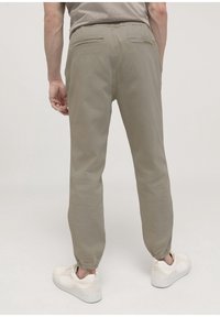 Ljusbeige joggerbyxor med elastiska mudd, två bakfickor och en dragsko i midjan. Bärs med vita sneakers. Slät textur.