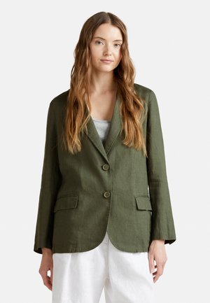 Blazer de lino verde oliva con un corte relajado, presenta dos botones, solapas de muesca y bolsillos frontales. Combinado con una blusa gris claro.