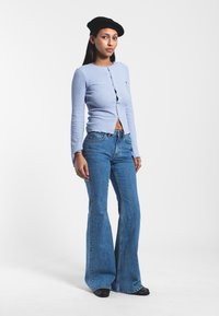 Light blue ribbed cardigan with long sleeves and front buttons, paired with blue flared jeans. Black beret and black footwear complete the outfit.