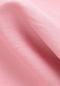 Textilie v světle růžové barvě s texturovaným, diagonálně žebrovaným vzorem. Měkký povrch s mírným leskem, složená tak, aby ukázala hloubku a vrstvy.