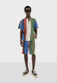 Ensemble de chemise à manches courtes et de shorts à rayures multicolores (bleu, vert, rouge, beige), avec de légers boutons et des baskets marron.