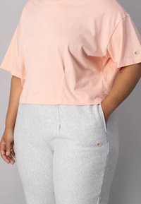 Lys rosa cropped t-shirt med korte ærmer, lavet af blødt stof. Kombineret med grå sweatpants med sidelommer og logo-detalje.