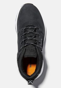 Zapatilla deportiva negra con parte superior de ante, puntera redonda, cordones negros y plantilla naranja. Presenta una suela de goma blanca y acentos de malla negra.