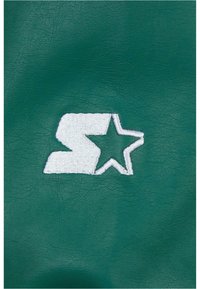 Teal sünteetiline nahk, millel on valge tikandiga logo, millel on stiliseeritud täht 'S' ja tähtkujuline element, näidates sujuvat tekstuuri.