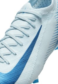 Botín de fútbol azul claro con parte superior texturizada, que presenta un gran swoosh azul y taquetes cónicos para tracción. Los cordones son de color azul claro.