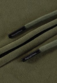 Felpa di color verde oliva con finitura testurizzata, caratterizzata da zip nere a contrasto con etichetta "RekigWear" e cordini intrecciati.
