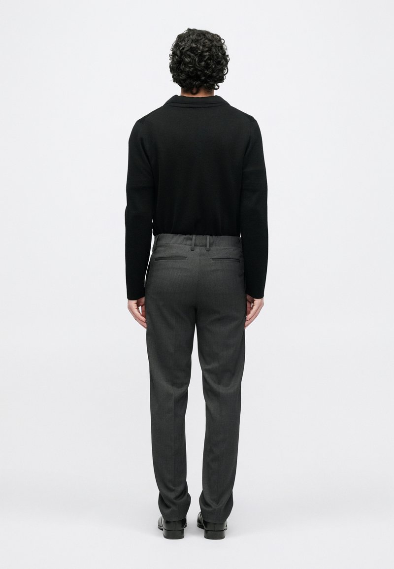Black long-sleeve shirt paired with gray trousers. Trousers feature a tailored fit and back pockets, designed for a streamlined look.