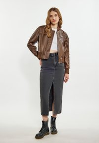 Jachetă bomber din piele maro cu manșete cu nervuri, asortată cu o fustă din denim negru cu talie înaltă, cu o fanta frontală, și cizme negre cu șireturi.