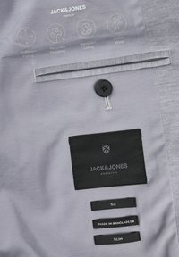 Sivi bi-streč jakenski material z črnim gumbom in žepi, na katerih so oznake: "Jack & Jones," velikost "52," ter "Narejeno v Bangladešu."