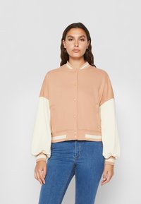 Persik ja koor cropped bomber-jakk, millel on soonikuga krae ja mansetid, nupuga kinnitamine ja kontrastsete varrukatega. Sile kangastekstuuri.