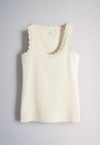 White sleeveless ribbed tank top with scalloped edges on neckline and armholes laid flat on a light surface.