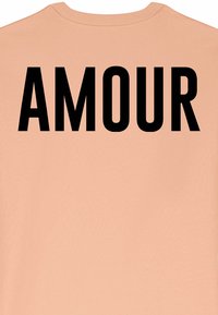 Persikinio atspalvio marškiniai, kurių nugaroje didelė juoda bloko rašmenų spauda žodžio "AMOUR". Atsitiktinio stiliaus medvilninė medžiaga, apvalios iškirptės dizainas.