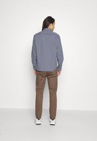 Karierter blau-weißer Langarmshirt, Rückansicht, kombiniert mit braunen Hosen und weißen Turnschuhen. Glatte Textur, normale Passform.