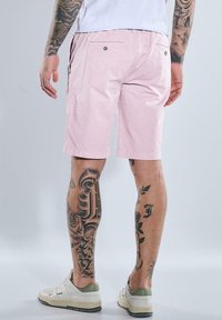 Pink cotton shorts with a flat front, two back pockets, and embroidered details. Worn with white sneakers featuring green accents.