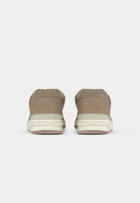 Beige kedas ar gludu augšējo daļu un teksturētām akcentiem, noapaļota zole un balta gumijas zole. Minimalistisks dizains ar diskrētu zīmolu.