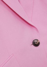 Růžový blazer s texturovanou tkaninou, klopami a lesklým černým knoflíkem. Obsahuje boční kapsu.