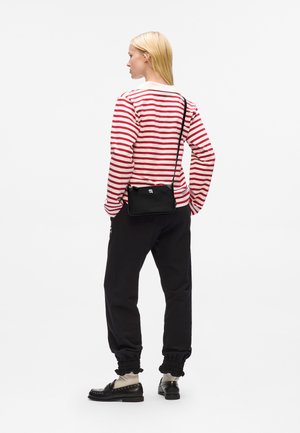 Black crossbody bag with a smooth texture and minimal design, paired with a red and white striped long-sleeve shirt and black joggers.