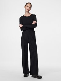 Blusa preta de mangas longas combinada com calças largas pretas com pregas. Apresenta uma textura suave e um ajuste clássico, complementado por sapatos pretos brilhantes.