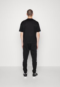 Svart bomullst-shirt med korta ärmar och svarta sweatsbyxor med vita sidodetaljer, kombinerat med svarta sneakers. Enkel, avslappnad passform.