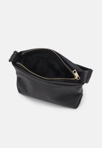 Pochette en cuir noir avec fermeture éclair dorée partiellement ouverte, montrant la doublure intérieure en tissu et une petite poche intérieure.