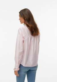 Lys rosa langermet skjorte med vertikale striper, knappede mansjetter og rynket detalj på baksiden. Brukes med denimjeans.