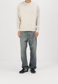 Felpa beige chiaro con scollo tondo, abbinata a jeans azzurri sbiaditi e a taglio largo. Completa il look un paio di sneakers nere con strisce bianche.