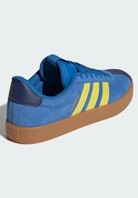 Sneakers blu in suede con strisce gialle e suola in gomma marrone. Include una punta testurizzata, linguetta imbottita e tallone in blu scuro.