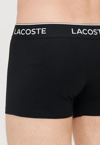 Crne pamučne bokserice s bijelim Lacoste logom na pojasu. Tkanina je glatka s prilagođenim dizajnom i kratkom dužinom nogavica.