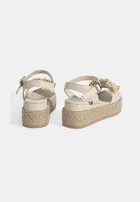 Beige platform sandalen met een verstelbare band, een geweven jute zool en decoratieve bloemaccenten aan de voorkant. Gladde leren bovenkant.