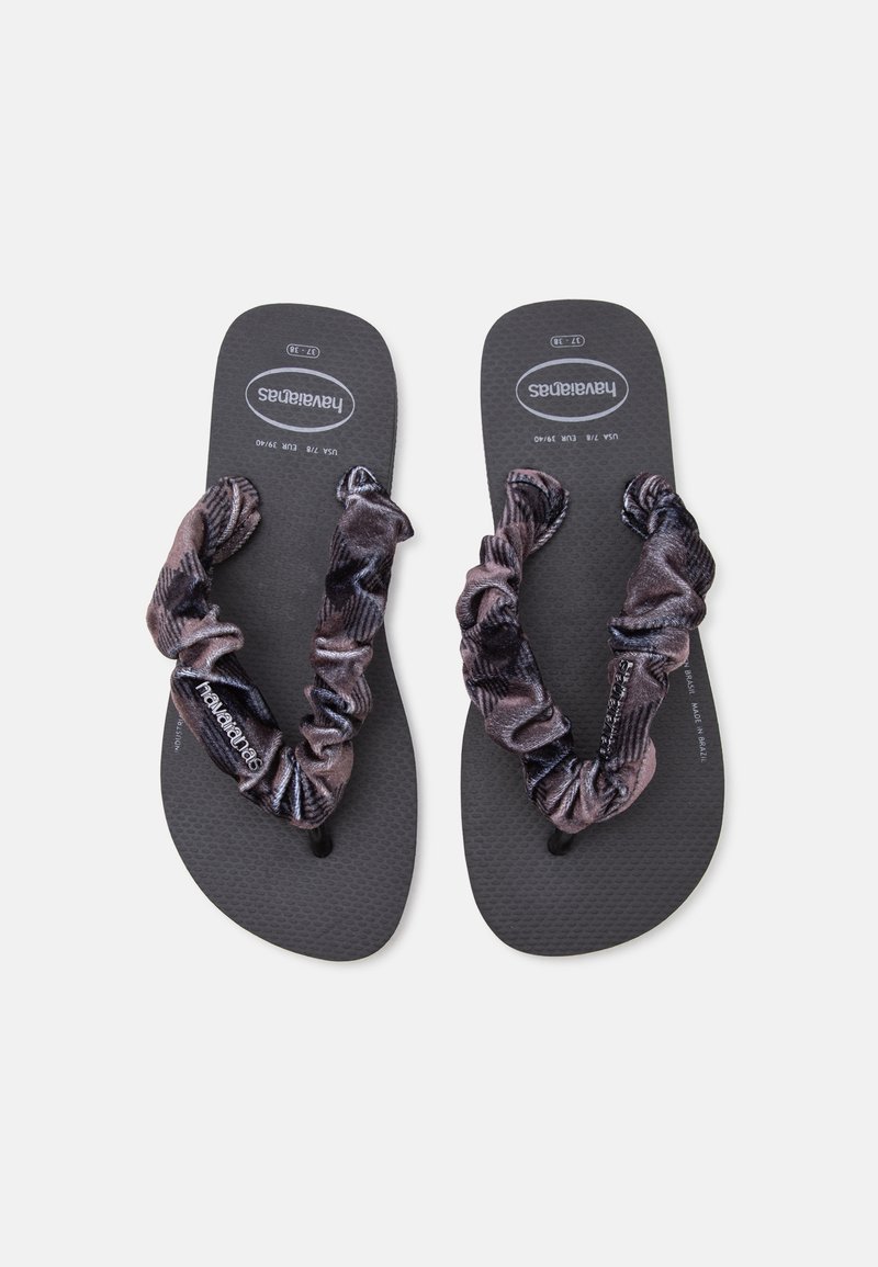 Двойка черни джапанки Havaianas с дрехнати тъмни текстилни каишки, разположени плоско с видим текст на подметката върху светлосив фон.