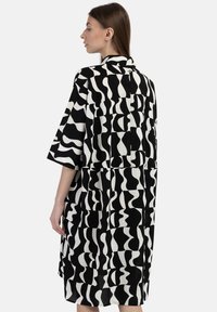 Schwarz-weiß gemustertes Kleid mit lockerer Passform, kurzen Ärmeln und Kragen. Verfügt über abstrakte Formen und einen leicht strukturierten Stoff.